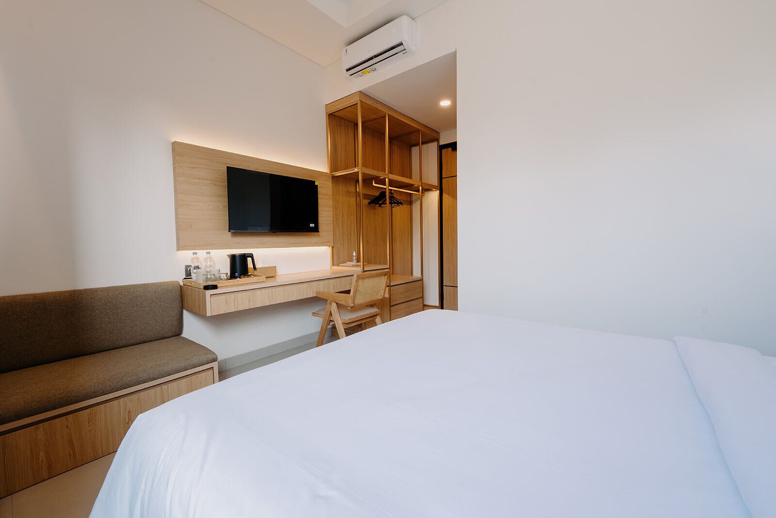 A hotel room with a bed, a desk with a flat-screen TV, a sofa, and a wardrobe.