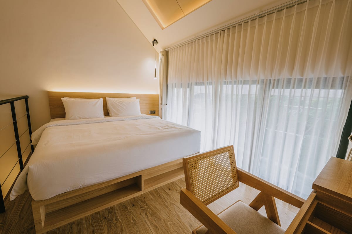 A modern hotel room with a large bed, wooden headboard, a wooden desk, and a chair.