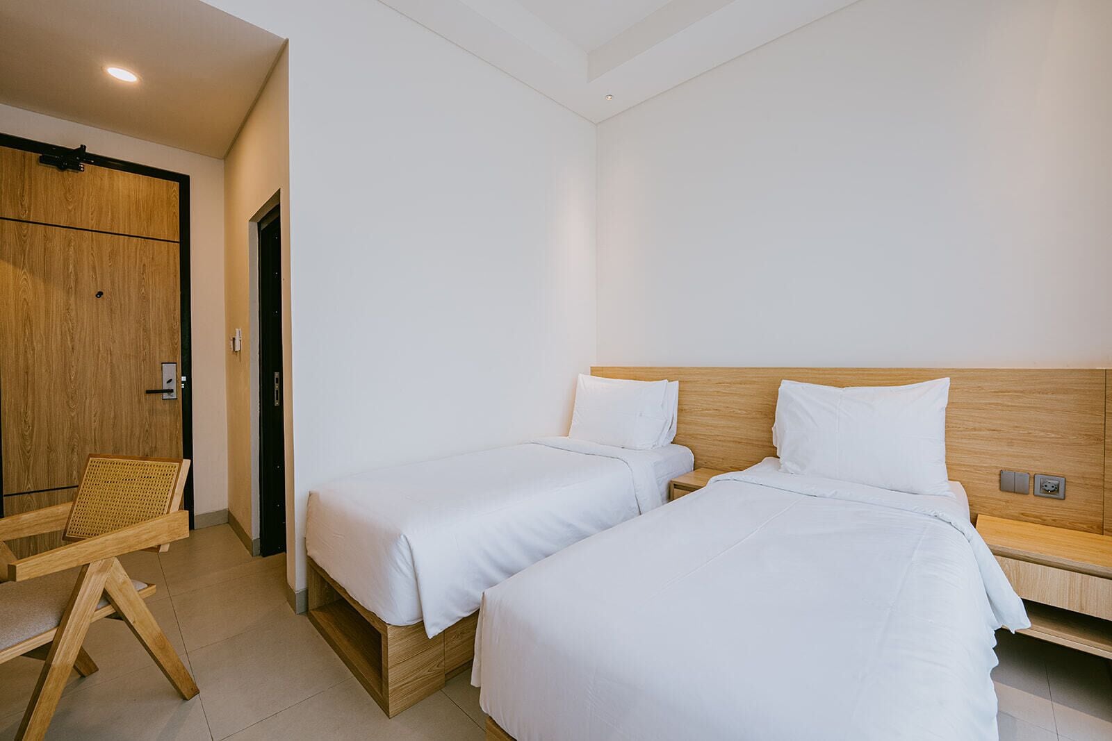 A hotel room with two single beds, a wooden chair, and a wardrobe.