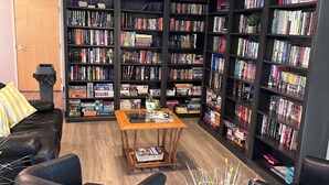 A library with multiple bookshelves, a leather sofa, a coffee table, and a potted plant. - Delightful 3-bedroom house with AC in San Tan Valley (San Tan Valley)
