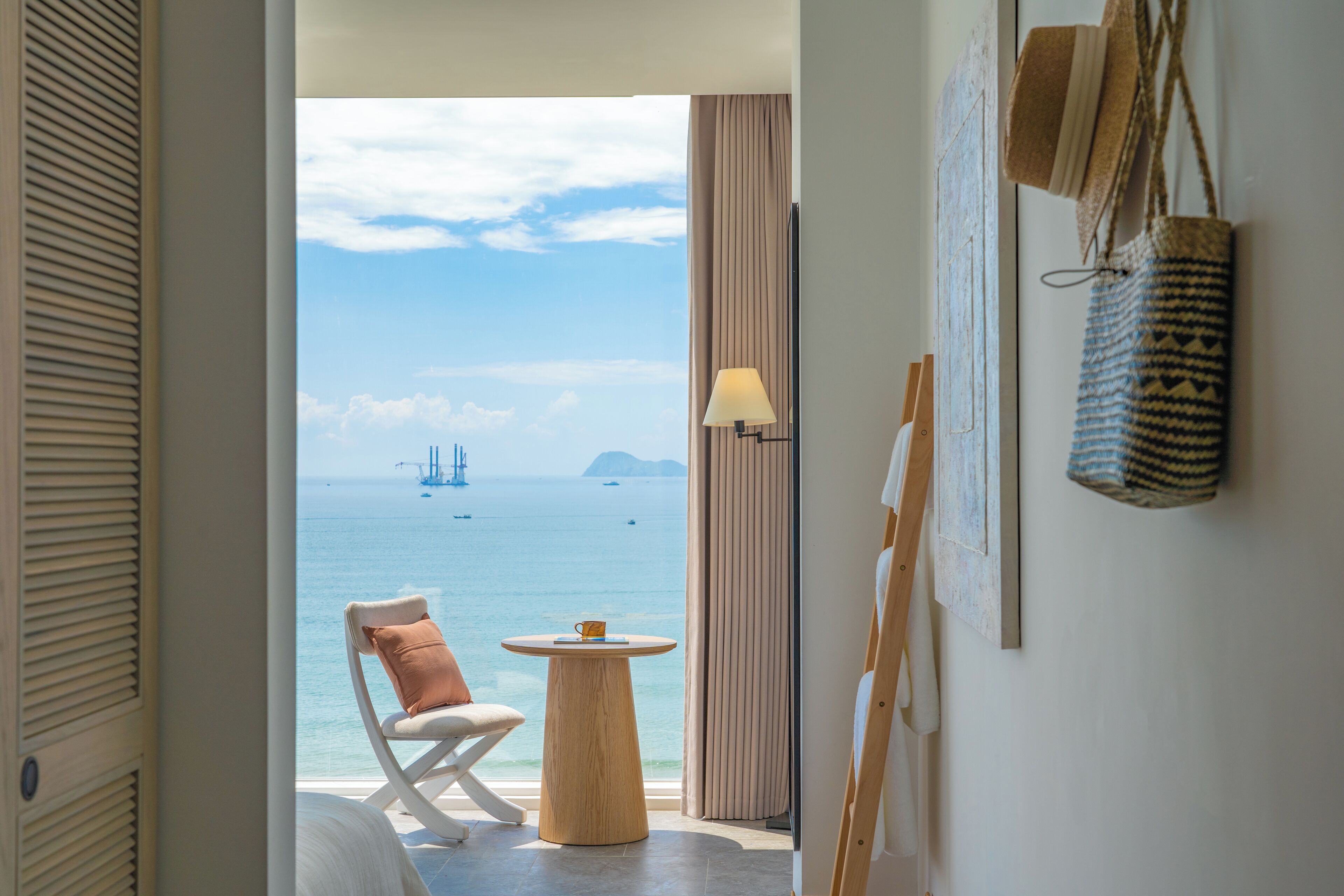 Een kamer met uitzicht op zee, een stoel, een tafeltje en een lamp.