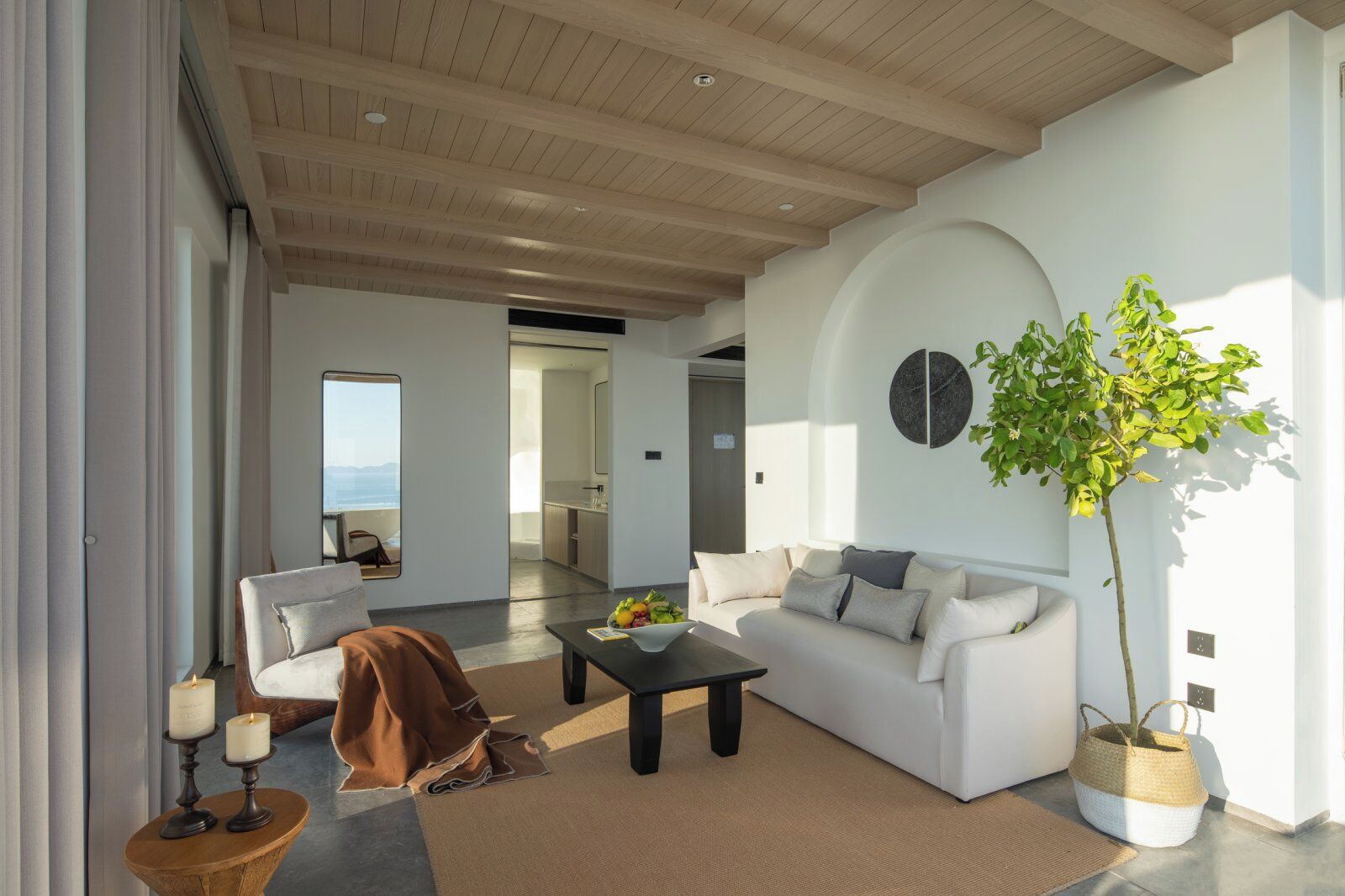 Una sala de estar moderna con un sofá blanco, una mesa de centro y un amplio ventanal con vistas a un balcón.