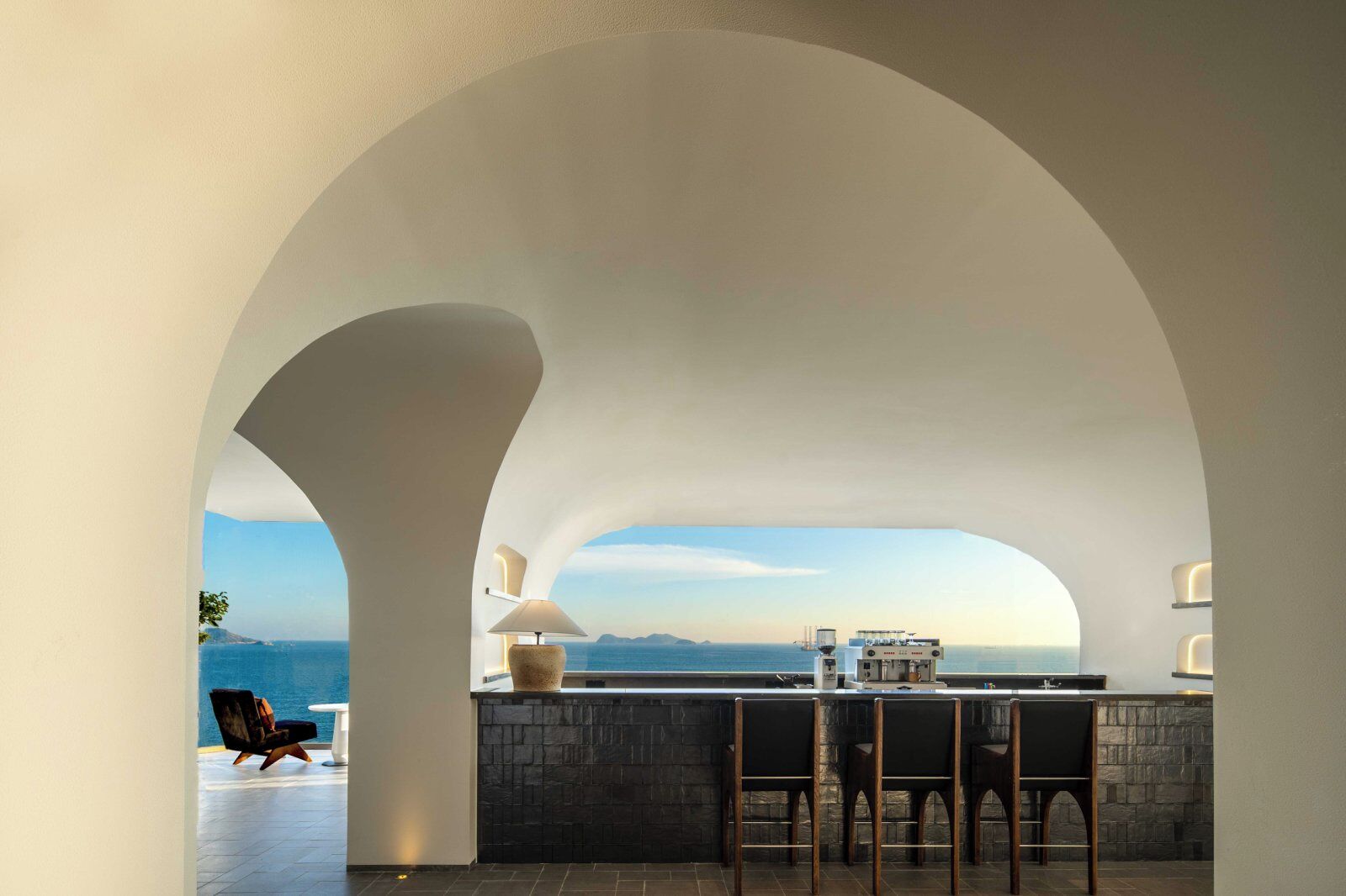 Cocina moderna con encimera de piedra y asientos en la barra, con vistas panorámicas al océano.