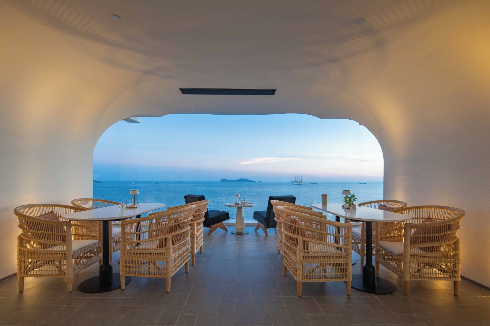 En inomhusrestaurang med möbler i rotting och utsikt över havet.
