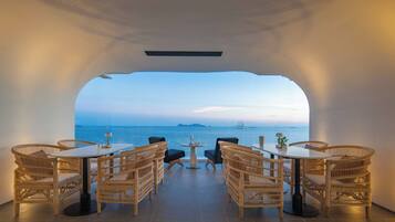 En inomhusrestaurang med möbler i rotting och utsikt över havet.