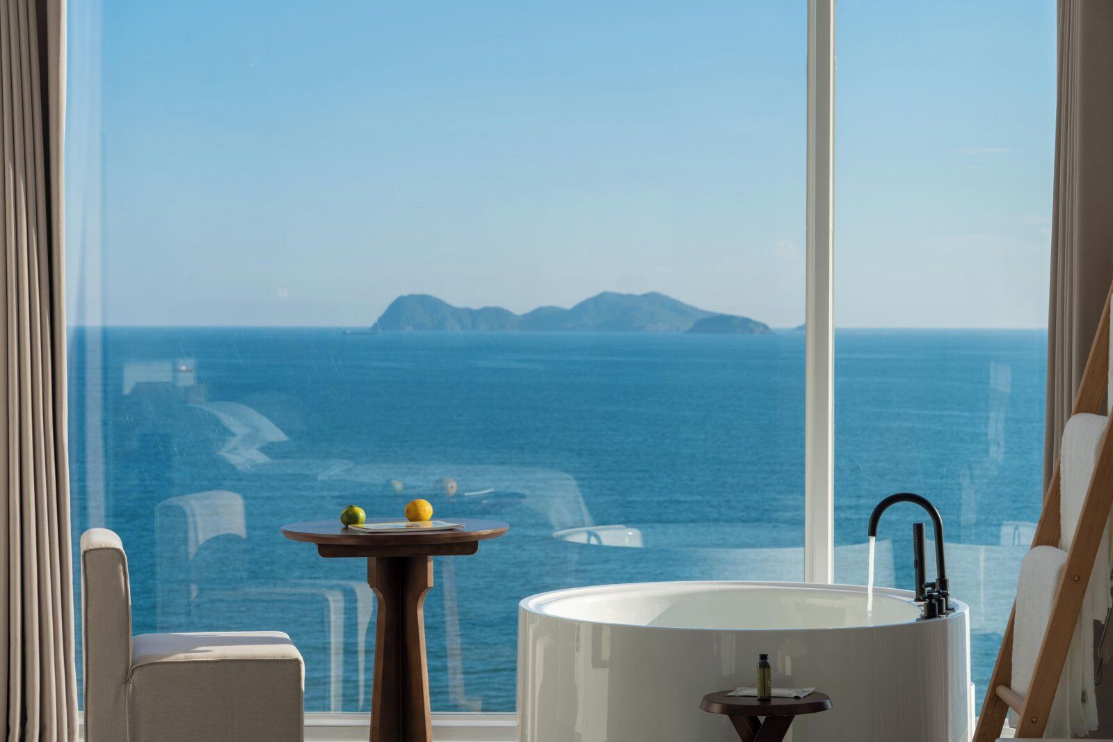 A bathroom with a bathtub, a small table with lemons, and a view of the sea.