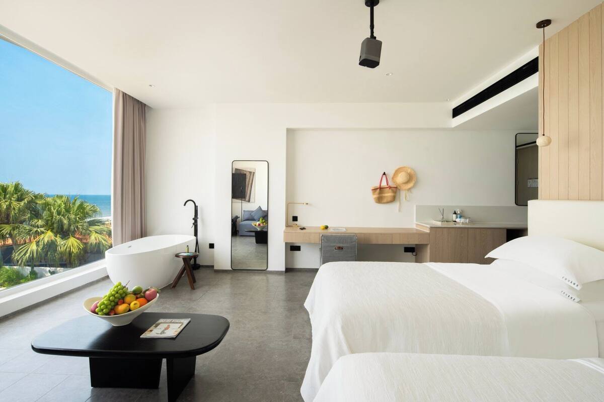 A hotel room with a large bed, a desk, a bathroom, and a view of the ocean.