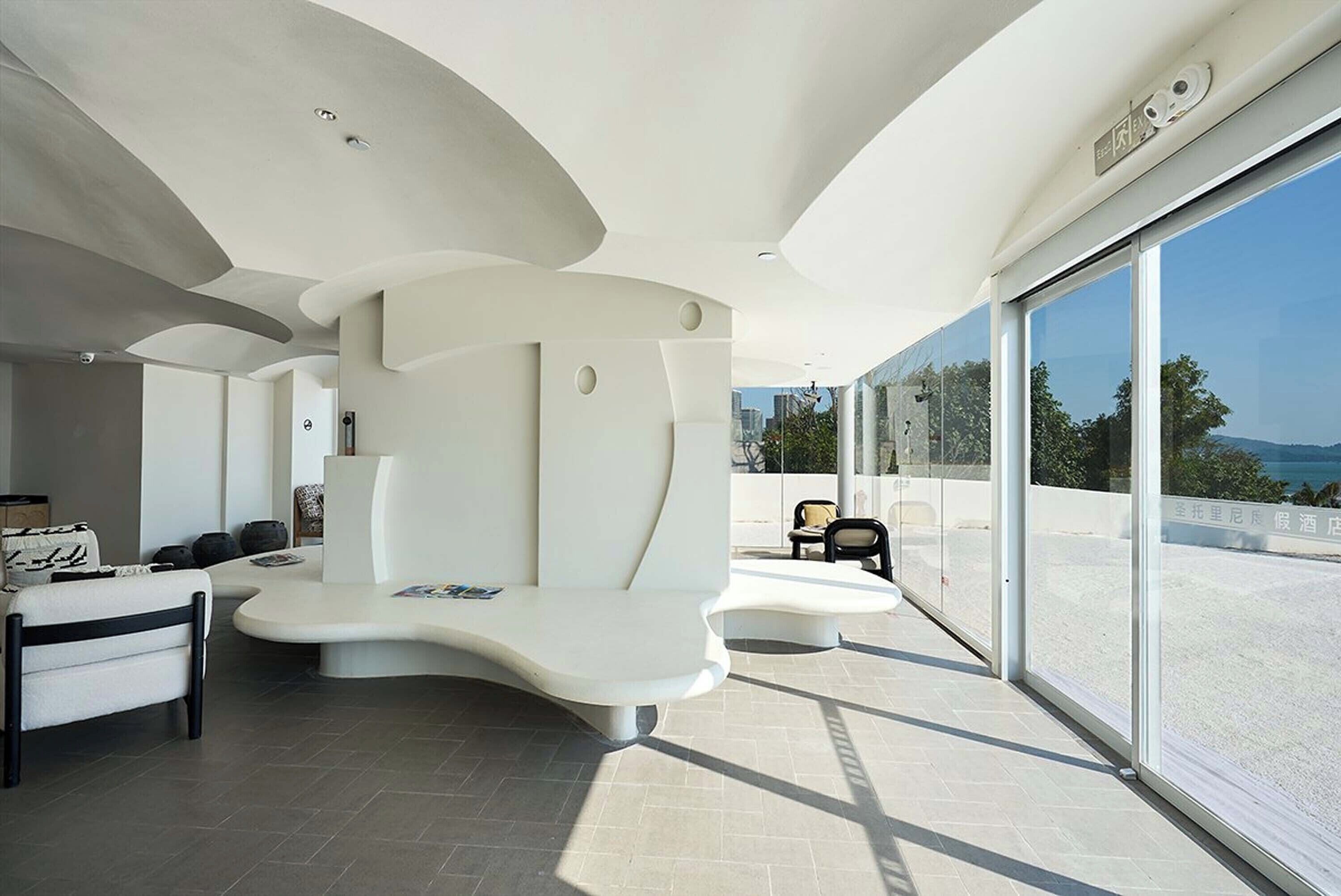 Un interior moderno con un banco blanco curvo, un sofá y un amplio ventanal con vistas al exterior.
