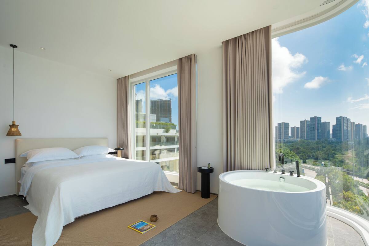 A modern hotel room with a large bed, a bathtub, and a city view.