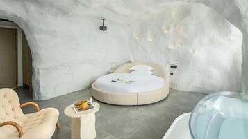 Un dormitorio moderno con una pared original de estilo hielo, una cama redonda, una bañera de vidrio y un sillón acogedor.