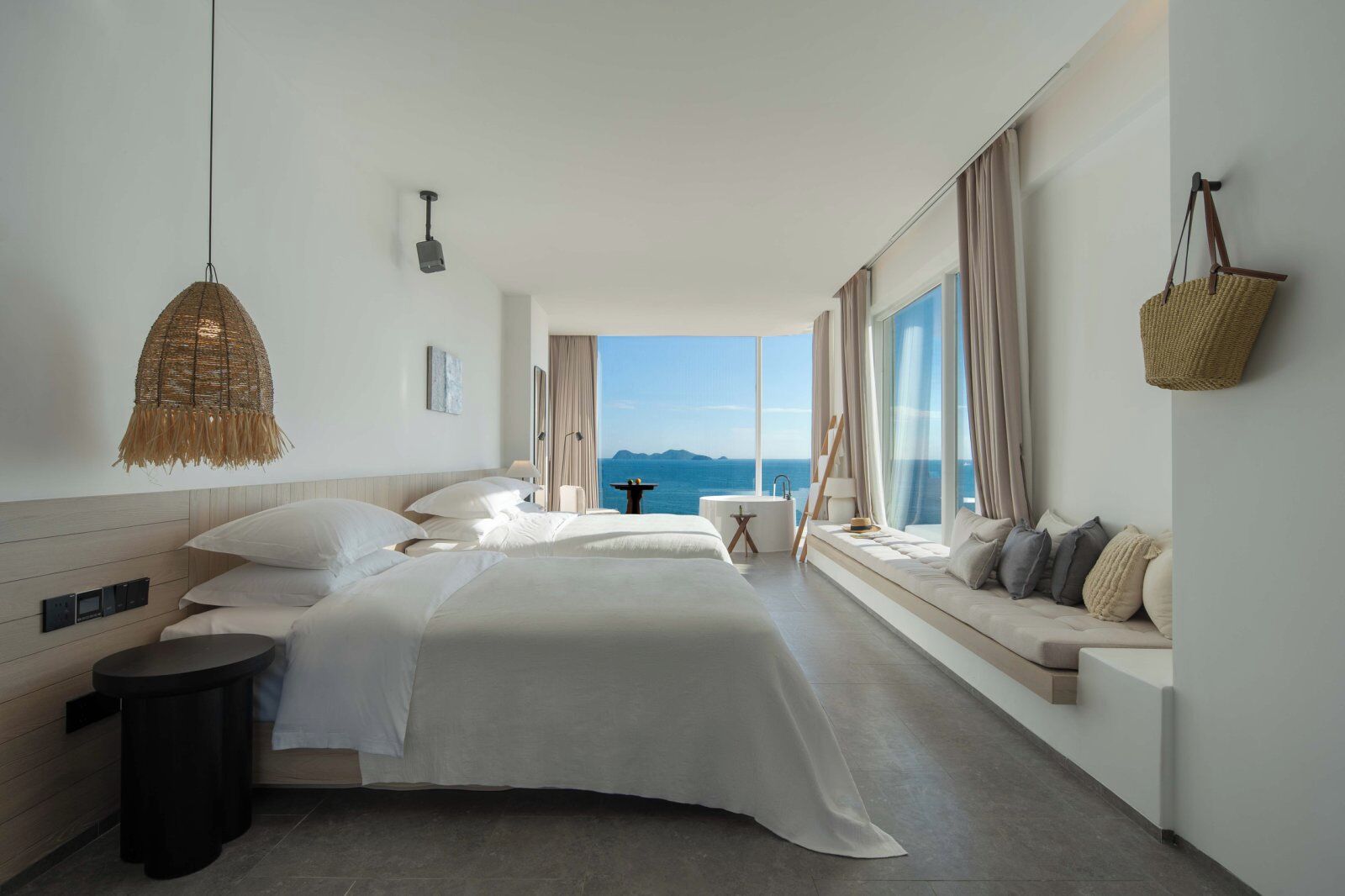 A modern hotel room with a large bed, a seating area with a view, and a balcony with a view of the sea.