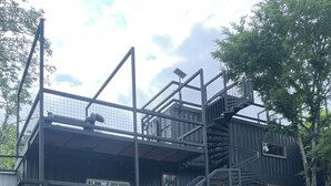 A modern building with a metal staircase, a fire pit, and a stone retaining wall.