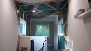 A narrow hallway with a geometric ceiling design, a red stool, and a white couch.