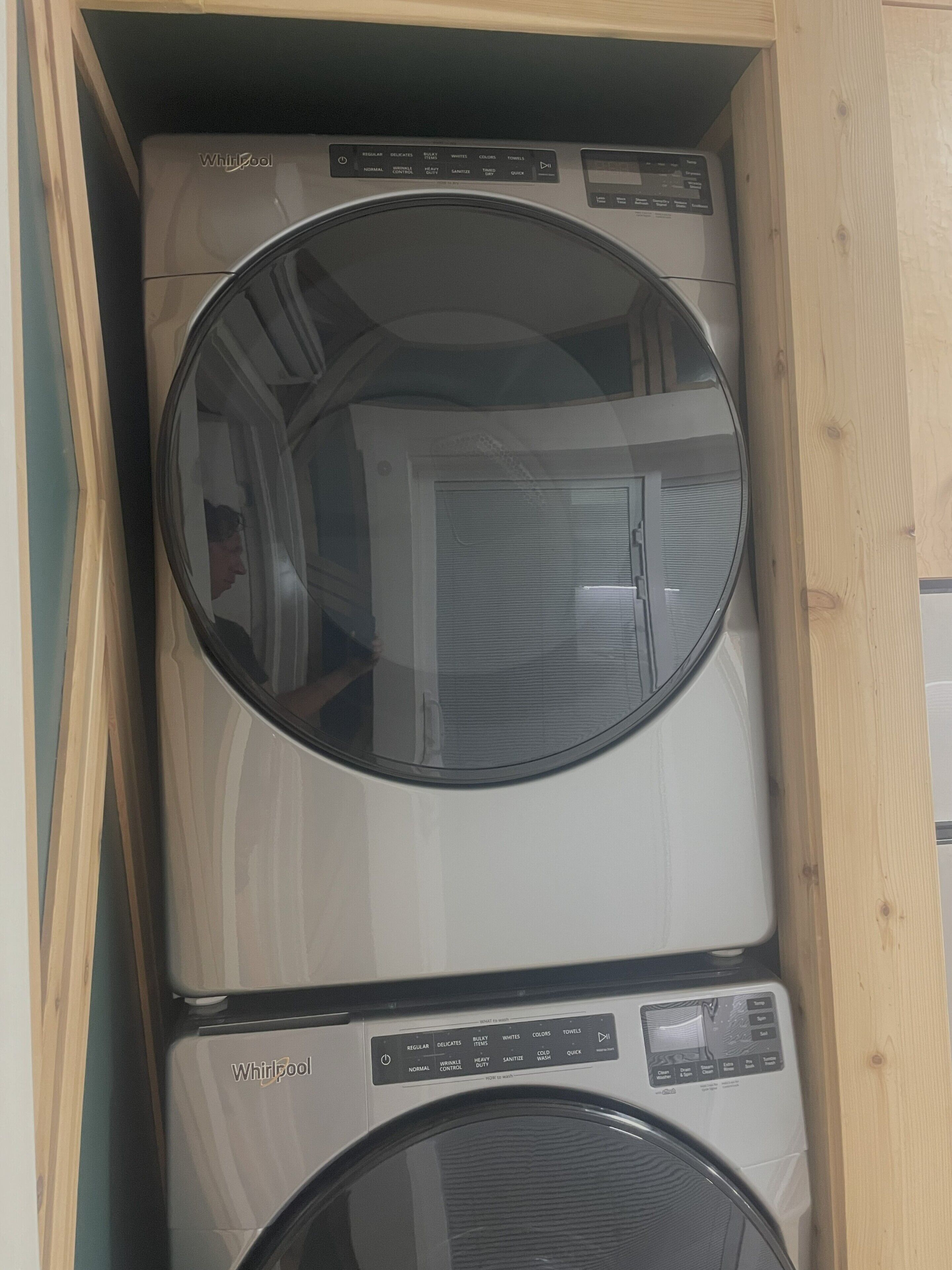 En kombinerad tvätt- och torkmaskin där maskinerna är staplade ovanpå varandra, med kontrollpaneler och en spegelblank glaslucka.