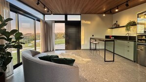 A modern kitchen with a large island, a dining area with a sofa, and a view of a green landscape through large windows. - Cozy house in the countryside of Garibaldi, close to wineries and restaurants (Garibaldi)