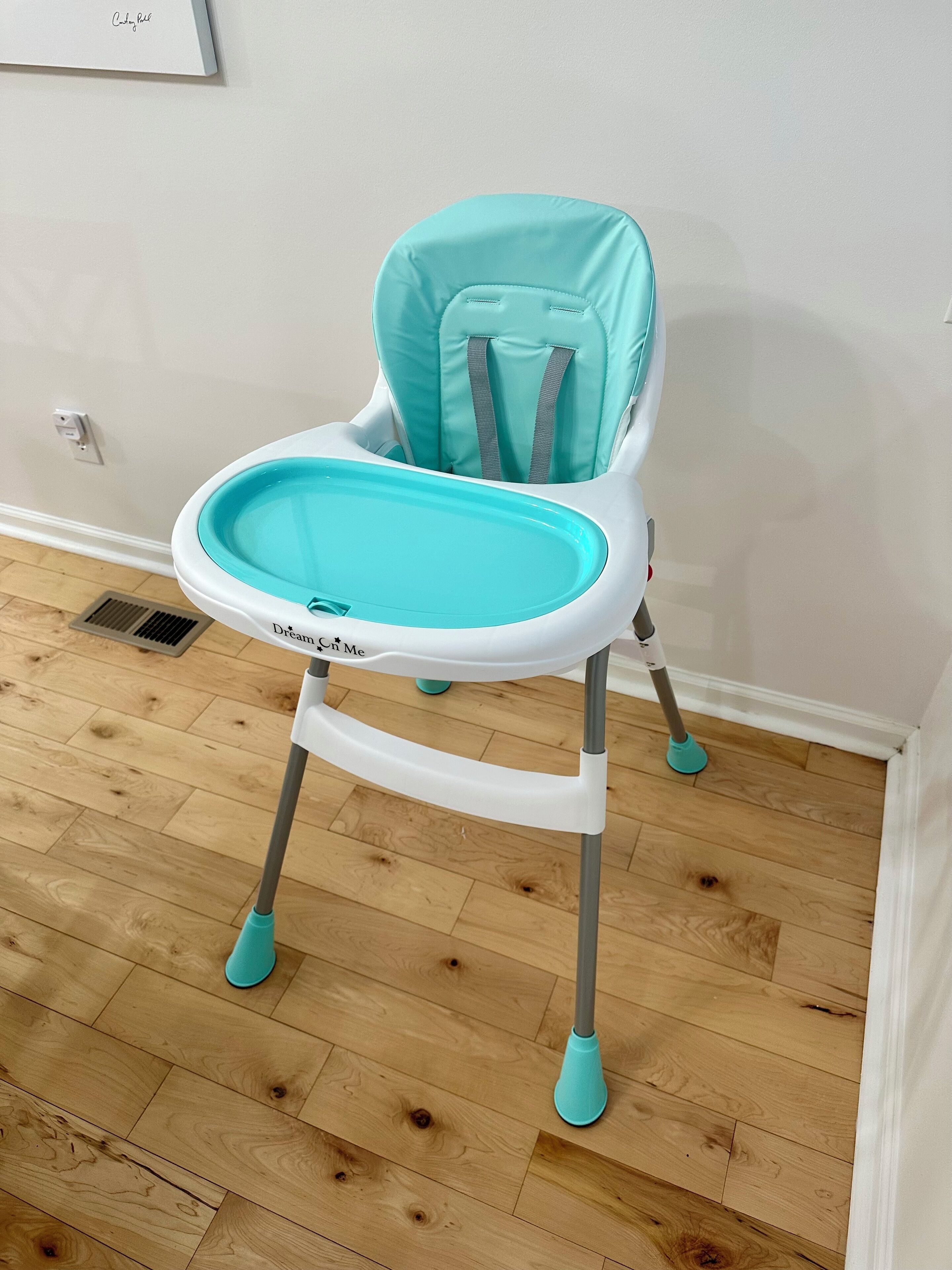 Een kinderstoel met een dienblad, geplaatst op een houten vloer met een witte muur op de achtergrond.