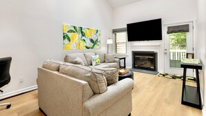Ein modernes Wohnzimmer mit einem beigen Sofa, einem flachbildfernseher über einem Kamin und einem großen Gemälde mit Zitronen an der Wand.