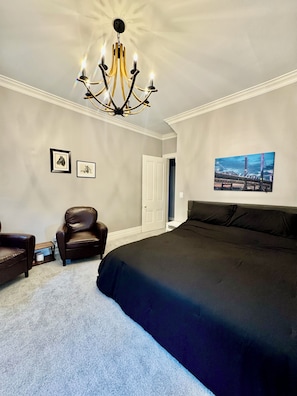 A bedroom with a large bed, a chandelier, a door, and a framed picture on the wall.