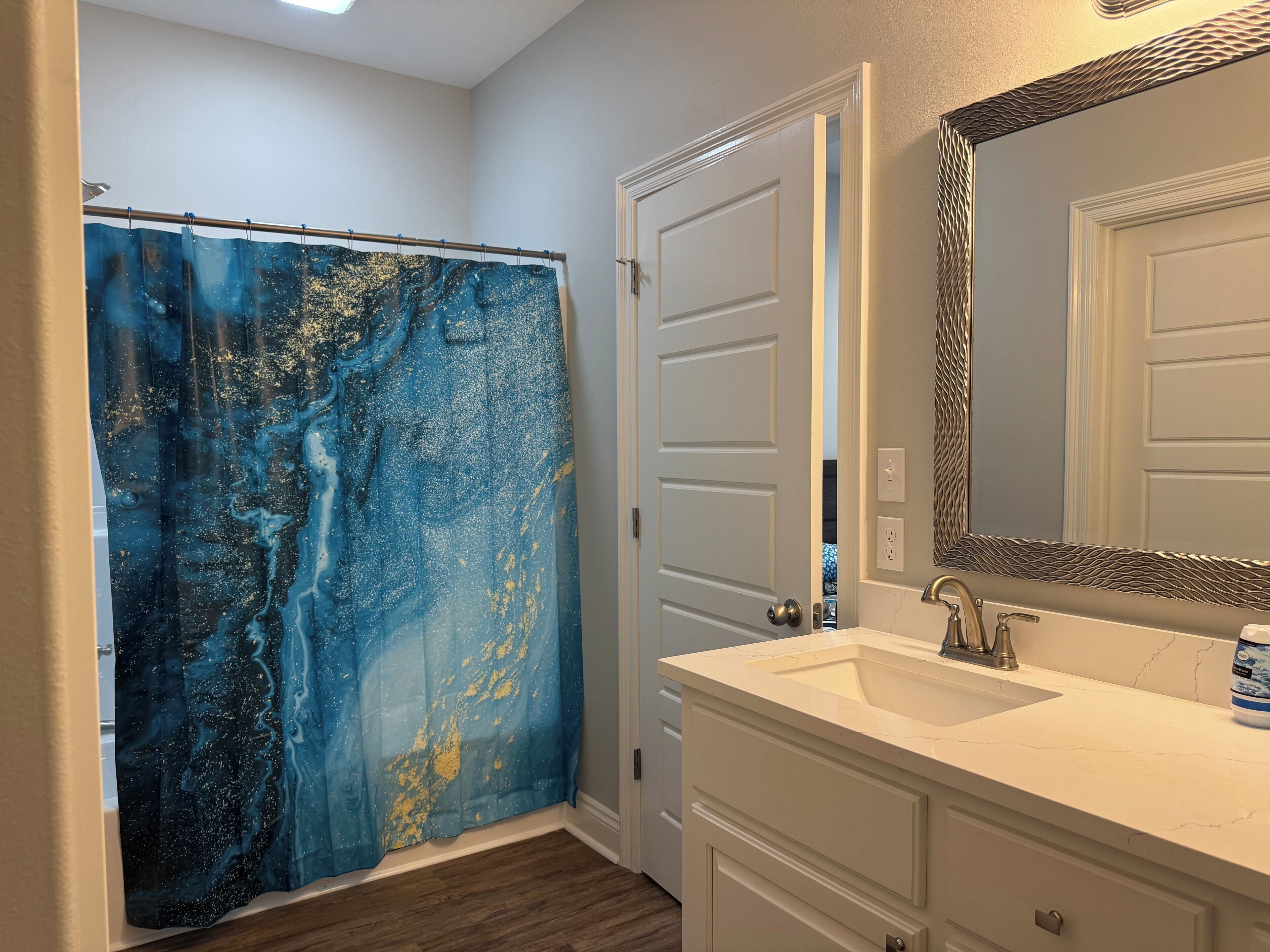 A bathroom with a white vanity, a large mirror, and a shower curtain with a blue and gold design.