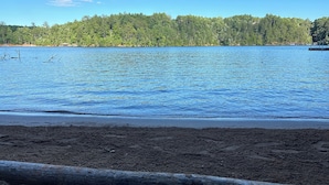 Une plage avec un tronc d’arbre en premier plan et une côte bordée d’une forêt en arrière-plan.