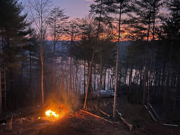 A forest with a campfire and a vehicle in the background. - Non-smoking lake house with private beach, dock and kayaks (Nebo)