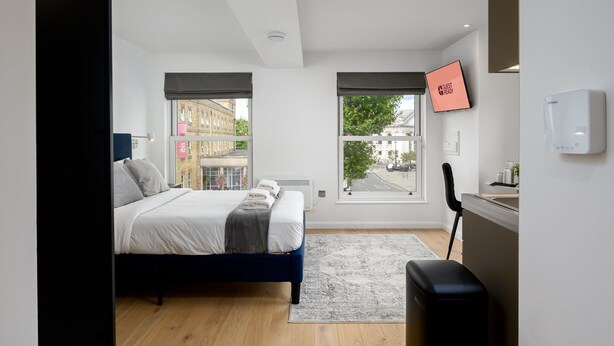 Une chambre d’hôtel moderne équipée d’un lit, d’un bureau, d’une chaise, d’une fenêtre et d’un téléviseur fixé au mur.