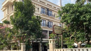 Un hotel de varios pisos con fachada color crema, balcones y un letrero que indica que está en venta.