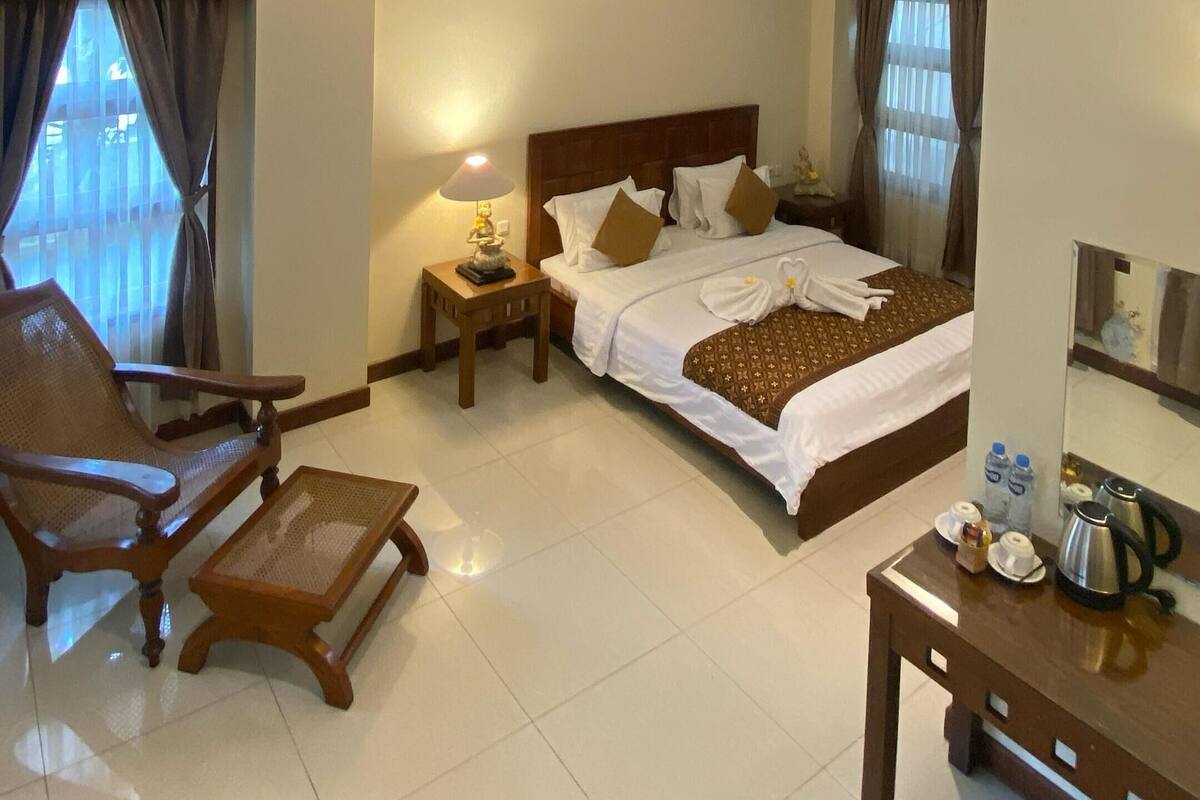 A hotel room with a bed, a chair, a small table, and a mirror.