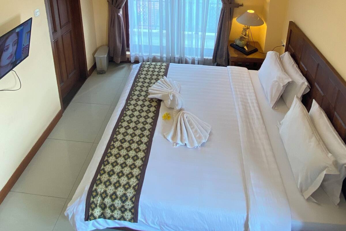 A hotel room with a large bed, a TV, an air conditioner, and a view through the window.