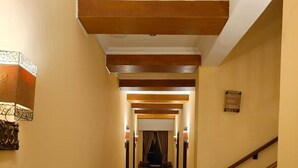 Un pasillo largo y estrecho con piso pulido, vigas de madera en el techo y una escalera a la derecha.