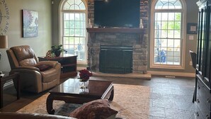 A spacious living room with a stone fireplace, leather furniture, and a ceiling fan.
