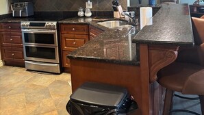 A kitchen with wooden cabinets, a stainless steel oven, a granite countertop, and a trash can.