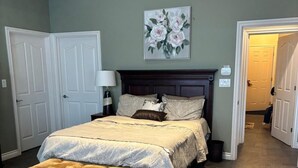 A bedroom with a large bed, a nightstand, a ceiling fan, and a door leading to another room.