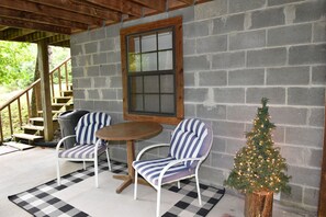 A covered patio with two striped chairs, a small table, a Christmas tree, and a wooden staircase.