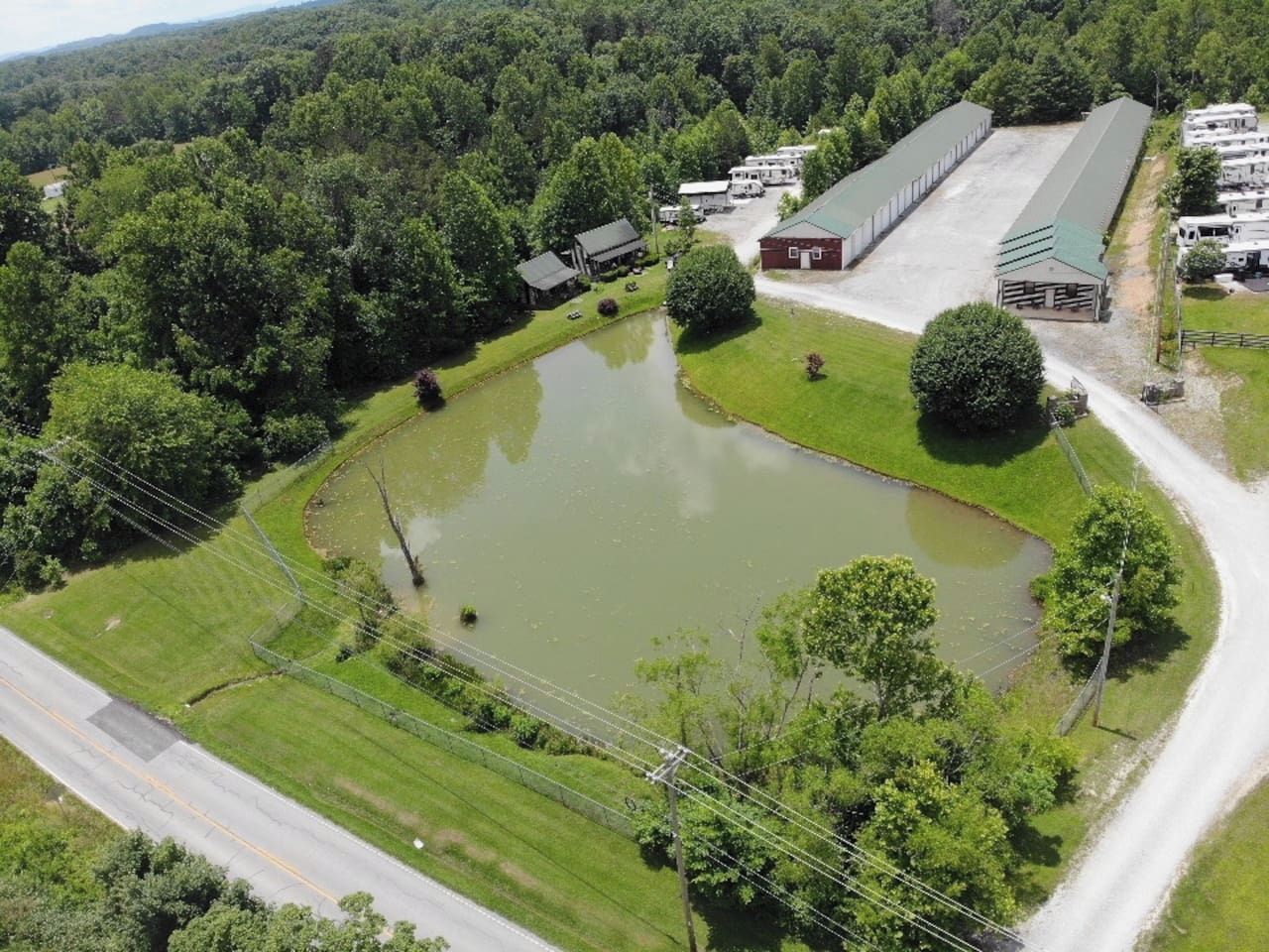 An aerial view of a property with a large pond, a barn, and a road.