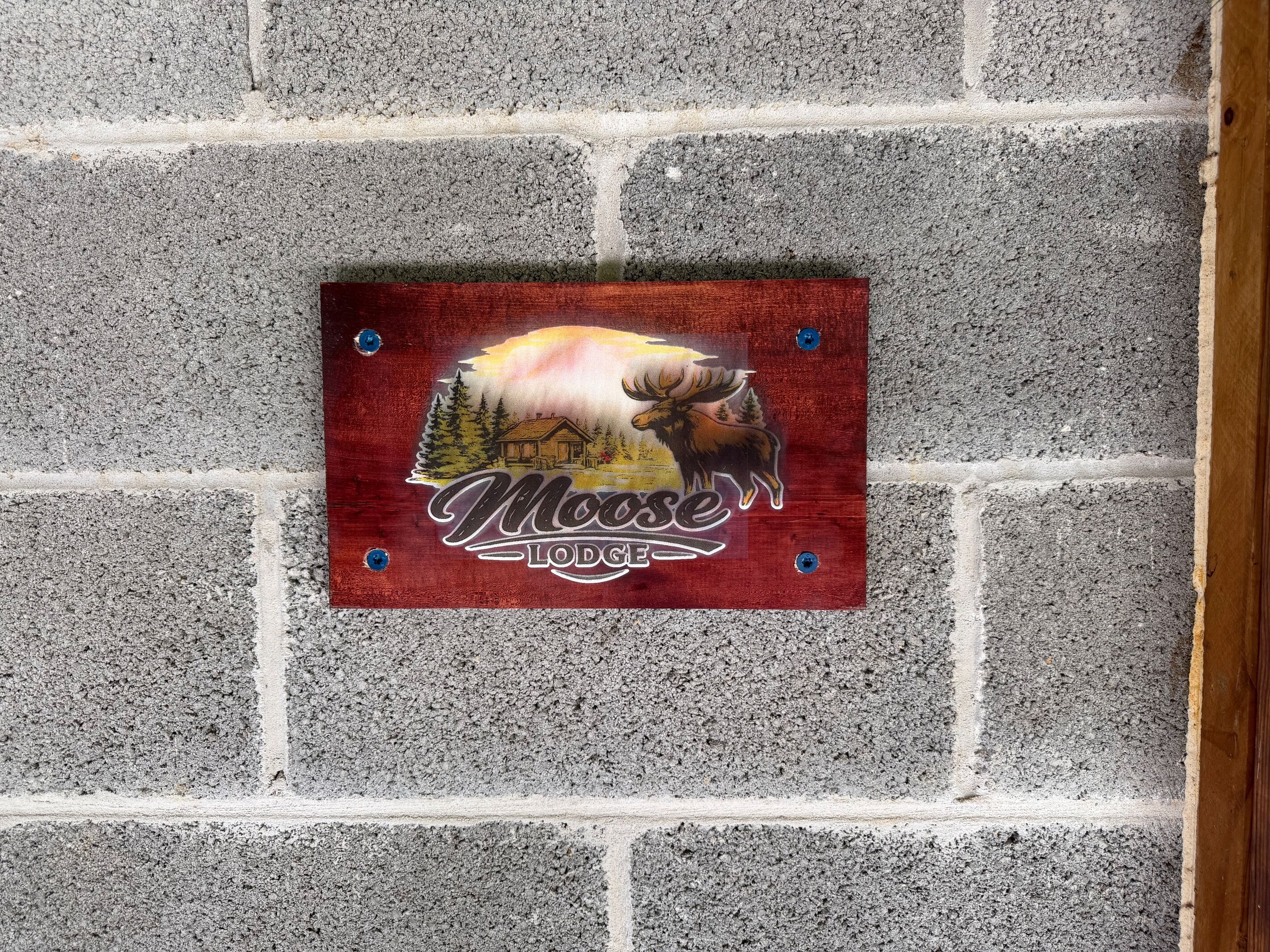 A wooden sign with a moose and lodge logo on a brick wall.