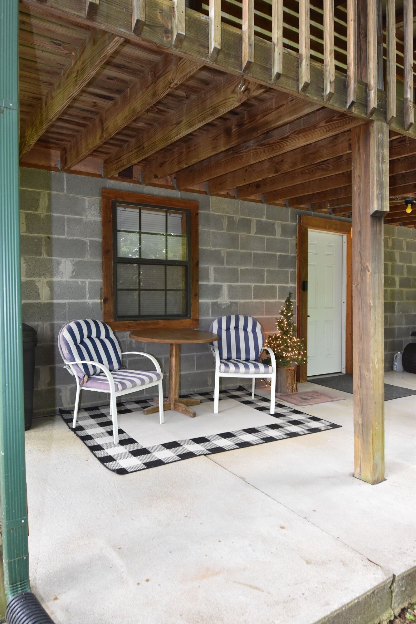 Une véranda avec deux chaises à rayures, une table en bois et un mur en briques.