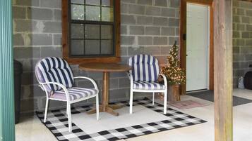 Une véranda avec deux chaises à rayures, une table en bois et un mur en briques.