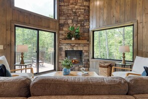 A cozy living room with a stone fireplace, large windows, and a view of the outdoors. - Luxe Cabin w/ Hot Tub, Views & Game Room Sleeps 10 Do Good Holler by Avantstay (Cosby)