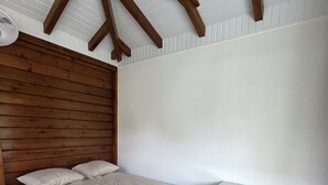 A bedroom with a wooden headboard, a single bed, a wooden nightstand with drawers, and a sloped ceiling with wooden beams. - L'Échappée Créole (Baie-Mahault)