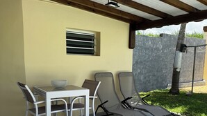 An outdoor patio with a table and chairs, a ceiling fan, and a wall-mounted air conditioning unit. - L'Échappée Créole (Baie-Mahault)