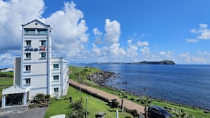 A coastal building with a stone facade, a clear view of the sea, and a distant island. - Sunrise Castle Pension (Seogwipo)