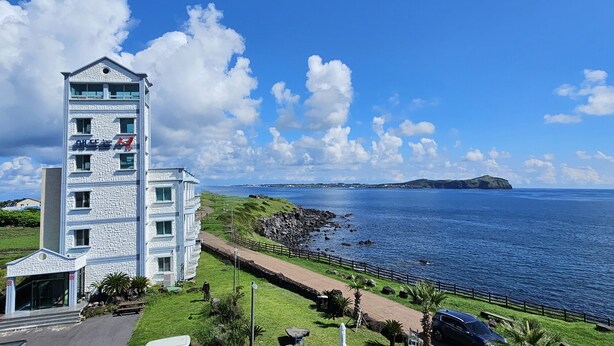 A coastal building with a stone facade, a clear view of the sea, and a distant island. - Sunrise Castle Pension (Seogwipo)