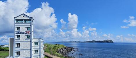 A coastal building with a stone facade, a clear view of the sea, and a distant island.
