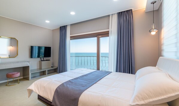 Una habitación de hotel moderna con una cama grande, un escritorio con televisor y vista al mar.