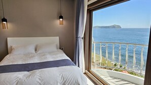 A bedroom with a large bed, two pendant lights, a view of the sea, and a balcony with a railing. - Sunrise Castle Pension (Seogwipo)