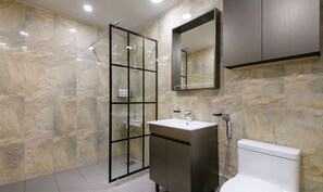 A modern bathroom with a glass-enclosed shower, a vanity with a sink, and a toilet. - Sunrise Castle Pension (Seogwipo)