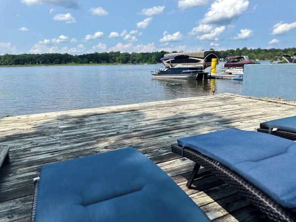 A wooden dock with lounge chairs and a covered boat.