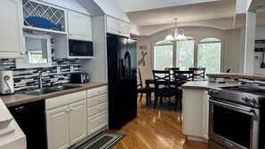 A modern kitchen with white cabinetry, a black refrigerator, a built-in oven, and a dining area with a table and chairs. - Wolf Lake Haven - Lakefront Sleeps 16 (Jackson)