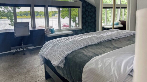 A bedroom with a large bed, a desk, and a view of a lake through large windows. - Wolf Lake Haven - Lakefront Sleeps 16 (Jackson)